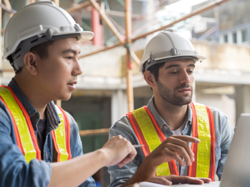 Dos hombres con cascos de seguridad revisan planes en una obra de construcción.