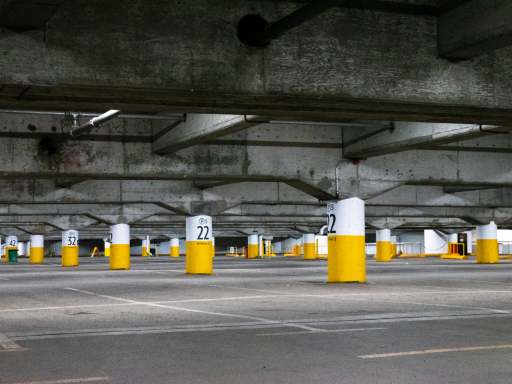 Vista de un aparcamiento subterráneo con columnas amarillas y blancas en el suelo.