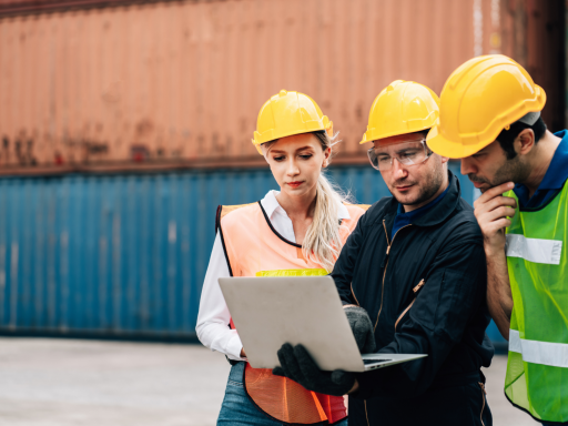Tres trabajadores en un puerto, revisando información en un portátil.