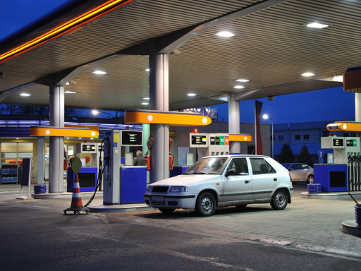Estación de servicio por la noche con varios surtidores y un coche blanco.