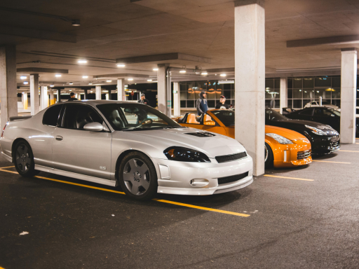 Coches estacionados en un aparcamiento, incluyendo un coche plateado y otro naranja.